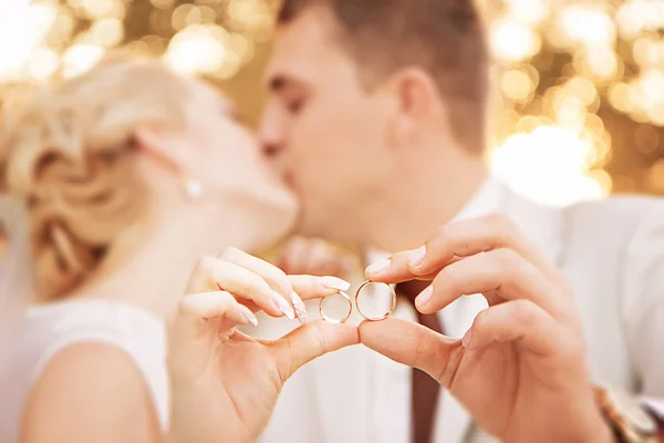 Två guld vigselringar på armarna på kyssar nygifta. Stockfoto