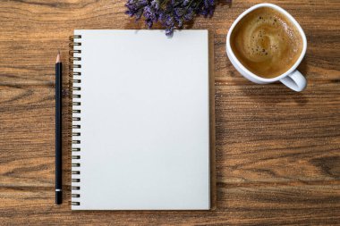 Tahta bir masanın üzerinde açık bir defter, bir kalem, bir fincan kahve ve bir buket çiçek var.