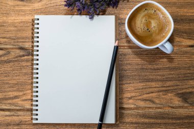 Tahta bir masanın üzerinde açık bir defter, üzerinde bir kalem, bir fincan kahve ve bir buket çiçek var..