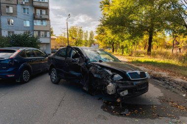 Trafik kazasından sonra ağır hasar görmüş siyah bir arabanın yakın çekimi. Ön tarafı tamamen ezilmiş, şiddetli vücut deformasyonuyla. Tekerlek hizalanmamış..