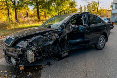 Trafik kazasından sonra ağır hasar görmüş siyah bir arabanın yakın çekimi. Ön tarafı tamamen ezilmiş, şiddetli vücut deformasyonuyla. Tekerlek hizalanmamış..