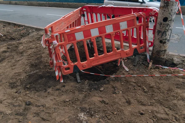 Yolun kenarına ya da derin bir deliğe yerleştirilmiş kırmızı plastik taşınabilir çit. Yerdeki açık delik tehlikeli bölgelerin yol onarımı ve çitlenmesi ihtiyacını gösteriyor..