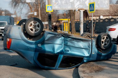Bir trafik kazasından sonra mavi bir yolcu arabası kaldırımlı bir yolda baş aşağı yatıyor. Şasinin yakın çekimi gösteriliyor. Güvenlik, sigorta, trafik ve sonuçlar konuları.