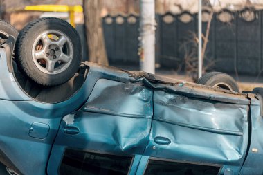 Bir trafik kazasından sonra mavi bir yolcu arabası kaldırımlı bir yolda baş aşağı yatıyor. Şasinin yakın çekimi gösteriliyor. Güvenlik, sigorta, trafik ve sonuçlar konuları.
