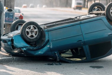 Bir trafik kazasından sonra mavi bir yolcu arabası kaldırımlı bir yolda baş aşağı yatıyor. Şasinin yakın çekimi gösteriliyor. Güvenlik, sigorta, trafik ve sonuçlar konuları.