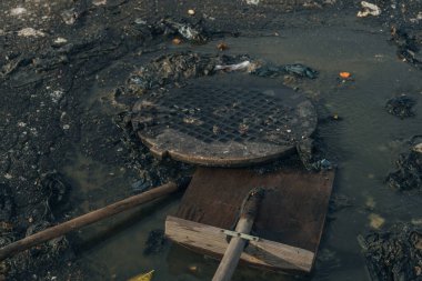 Kirli, yağlı bir su yüzeyi ve metal rögar kapağı dokusu. Kentsel ve sorunlu imaj. Ekoloji, çevre kirliliği ve kamu hizmetleri konularında. Kanalizasyon çıkışı.