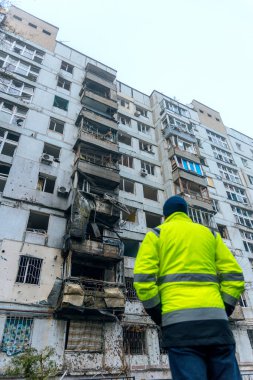 Bir adam, bir füze saldırısının ya da bir yerleşim yerinin topçu bombardımanının sonrasına bakıyor. Duvarlarda ve camlarda şarapnel izleri var. Patlama dalgası yüzünden parçalanmış..