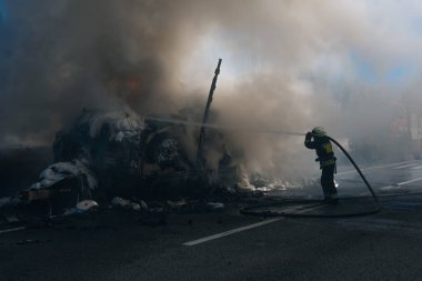 Üniformalı bir itfaiyeci güçlü bir su akışını yanan bir nesneye yönlendirir. Işığın ve gölgenin güçlü kontrastı durumun dramasını vurguluyor..