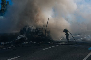 Üniformalı bir itfaiyeci güçlü bir su akışını yanan bir nesneye yönlendirir. Işığın ve gölgenin güçlü kontrastı durumun dramasını vurguluyor..