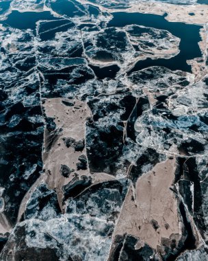 Doğal Doku: Sürüklenme sırasında buzun kırılganlığını ve yapısını gösteren dikey bir dron görüntüsü. Serin mavi ve toprak renkleri arasındaki zıtlık.