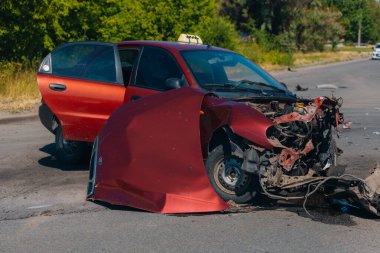 Ciddi bir trafik kazası: ciddi şekilde hasar görmüş kırmızı bir araba ve kaldırımda duran patlak bir lastik. Araba kafa kafaya çarpışma izleri gösteriyor. Patlamış motor ve kaput da dahil..