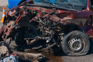 Ciddi bir trafik kazası: ciddi şekilde hasar görmüş kırmızı bir araba ve kaldırımda duran patlak bir lastik. Araba kafa kafaya çarpışma izleri gösteriyor. Patlamış motor ve kaput da dahil..