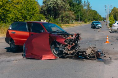 Ciddi bir trafik kazası: ciddi şekilde hasar görmüş kırmızı bir araba ve kaldırımda duran patlak bir lastik. Araba kafa kafaya çarpışma izleri gösteriyor. Patlamış motor ve kaput da dahil..