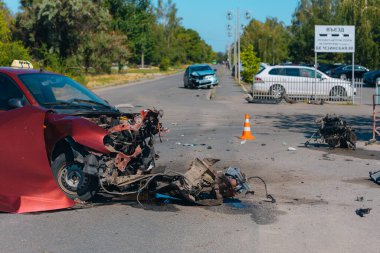 Ciddi bir trafik kazası: ciddi şekilde hasar görmüş kırmızı bir araba ve kaldırımda duran patlak bir lastik. Araba kafa kafaya çarpışma izleri gösteriyor. Patlamış motor ve kaput da dahil..