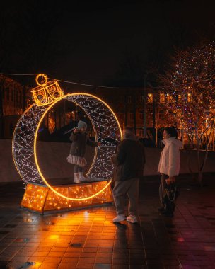 Gece aydınlatması: kış tatilleri boyunca parlak ve dekore edilmiş bir şehir caddesi. Çok renkli LED ışıklar ve dekorasyonlar. İnsanlar şehir merkezinde dolaşırken neşeli bir atmosfer..