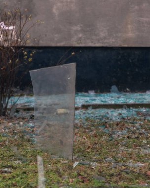 Keskin bir kırık cam parçasının yakın plan görüntüsü yerden dikey olarak çıkıntılı. Cam parçaları, çatışmanın trajik sonuçlarını vurgulayan bir bombardıman ya da patlamanın sonucu..