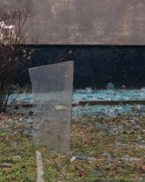 Keskin bir kırık cam parçasının yakın plan görüntüsü yerden dikey olarak çıkıntılı. Cam parçaları, çatışmanın trajik sonuçlarını vurgulayan bir bombardıman ya da patlamanın sonucu..