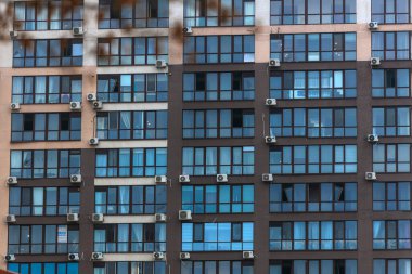 Modern çok katlı bir konut binasının ön cephesinin bir parçası. Bina bej ve kahverengi tonlarda tamamlanmıştır. Yeni kentsel gelişmenin bir parçası. Pencereler kırılmış..