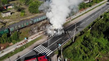 Bir İHA 'dan hava görüntüsü: İtfaiyeciler yol kenarındaki büyük bir yangını söndürür. Yanan binadan yoğun beyaz duman yükseliyor.. 