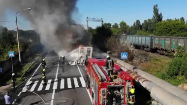 Bir İHA 'dan hava görüntüsü: İtfaiyeciler yol kenarındaki büyük bir yangını söndürür. Yanan binadan yoğun beyaz duman yükseliyor.. 
