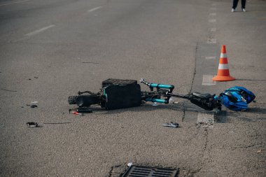 Elektrikli scooter kazası: hasarlı bir scooter ve kaldırımda duran kırık bir kask. Mikrohareketlilik kazalarının sonuçları, tehlike kavramı ve yol güvenliği..