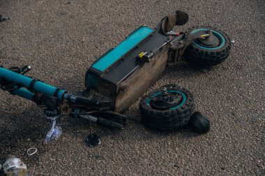 Elektrikli scooter kazası: hasarlı bir scooter ve kaldırımda duran kırık bir kask. Mikrohareketlilik kazalarının sonuçları, tehlike kavramı ve yol güvenliği..
