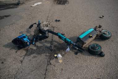 Elektrikli scooter kazası: hasarlı bir scooter ve kaldırımda duran kırık bir kask. Mikrohareketlilik kazalarının sonuçları, tehlike kavramı ve yol güvenliği..