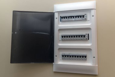 Duvara monte edilmiş bir elektrik paneli ya da üç sıra devre kesici ve sigorta içeren açık siyah bir kapısı olan dağıtım kutusu. Bir evde ya da dairede elektriği yönetmek için gerekli ekipman. Elektrik, onarım, güvenlik ve teknoloji kavramı.