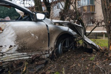Ciddi bir trafik kazasından sonra bir yolcu arabası büyük hasar gördü. Araba, yolun kenarındaki bir ağaca çarptı. Ön tarafı tamamen tahrip etti. Ön camı kırdı ve yere enkaz ve parçalar saçtı.