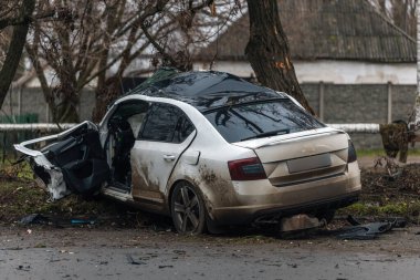 Ciddi bir trafik kazasından sonra bir yolcu arabası büyük hasar gördü. Araba, yolun kenarındaki bir ağaca çarptı. Ön tarafı tamamen tahrip etti. Ön camı kırdı ve yere enkaz ve parçalar saçtı.