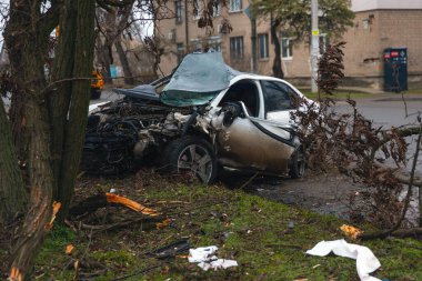 Ciddi bir trafik kazasından sonra bir yolcu arabası büyük hasar gördü. Araba, yolun kenarındaki bir ağaca çarptı. Ön tarafı tamamen tahrip etti. Ön camı kırdı ve yere enkaz ve parçalar saçtı.