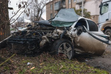 Ciddi bir trafik kazasından sonra bir yolcu arabası büyük hasar gördü. Araba, yolun kenarındaki bir ağaca çarptı. Ön tarafı tamamen tahrip etti. Ön camı kırdı ve yere enkaz ve parçalar saçtı.