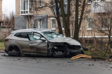 Şiddetli bir kazadan sonra, bir şehir caddesinde meydana gelen çarpışmadan sonra ön yüzünde feci hasar olan gri bir SUV. Kaput buruşmuş, lastik yerinden çıkmış, ön cam kırılmış ve kapı açık ve deforme olmuş..