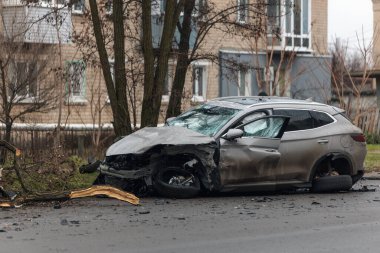 Şiddetli bir kazadan sonra, bir şehir caddesinde meydana gelen çarpışmadan sonra ön yüzünde feci hasar olan gri bir SUV. Kaput buruşmuş, lastik yerinden çıkmış, ön cam kırılmış ve kapı açık ve deforme olmuş..