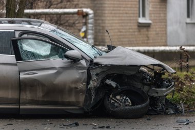 Şiddetli bir kazadan sonra, bir şehir caddesinde meydana gelen çarpışmadan sonra ön yüzünde feci hasar olan gri bir SUV. Kaput buruşmuş, lastik yerinden çıkmış, ön cam kırılmış ve kapı açık ve deforme olmuş..
