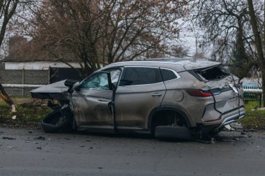 Şiddetli bir kazadan sonra, bir şehir caddesinde meydana gelen çarpışmadan sonra ön yüzünde feci hasar olan gri bir SUV. Kaput buruşmuş, lastik yerinden çıkmış, ön cam kırılmış ve kapı açık ve deforme olmuş..