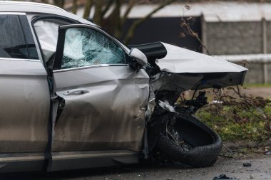 Şiddetli bir kazadan sonra, bir şehir caddesinde meydana gelen çarpışmadan sonra ön yüzünde feci hasar olan gri bir SUV. Kaput buruşmuş, lastik yerinden çıkmış, ön cam kırılmış ve kapı açık ve deforme olmuş..