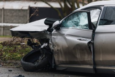 Şiddetli bir kazadan sonra, bir şehir caddesinde meydana gelen çarpışmadan sonra ön yüzünde feci hasar olan gri bir SUV. Kaput buruşmuş, lastik yerinden çıkmış, ön cam kırılmış ve kapı açık ve deforme olmuş..