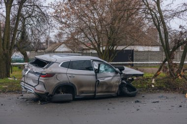Şiddetli bir kazadan sonra, bir şehir caddesinde meydana gelen çarpışmadan sonra ön yüzünde feci hasar olan gri bir SUV. Kaput buruşmuş, lastik yerinden çıkmış, ön cam kırılmış ve kapı açık ve deforme olmuş..