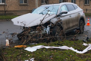 Şiddetli bir kazadan sonra, bir şehir caddesinde meydana gelen çarpışmadan sonra ön yüzünde feci hasar olan gri bir SUV. Kaput buruşmuş, lastik yerinden çıkmış, ön cam kırılmış ve kapı açık ve deforme olmuş..