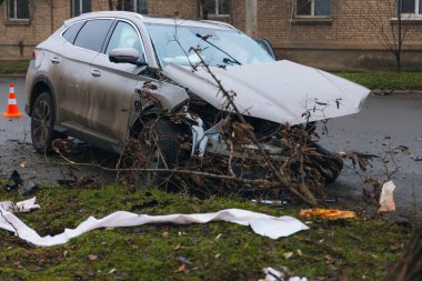 Şiddetli bir kazadan sonra, bir şehir caddesinde meydana gelen çarpışmadan sonra ön yüzünde feci hasar olan gri bir SUV. Kaput buruşmuş, lastik yerinden çıkmış, ön cam kırılmış ve kapı açık ve deforme olmuş..