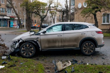 Şiddetli bir kazadan sonra, bir şehir caddesinde meydana gelen çarpışmadan sonra ön yüzünde feci hasar olan gri bir SUV. Kaput buruşmuş, lastik yerinden çıkmış, ön cam kırılmış ve kapı açık ve deforme olmuş..