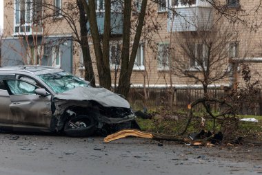 Şiddetli bir kazadan sonra, bir şehir caddesinde meydana gelen çarpışmadan sonra ön yüzünde feci hasar olan gri bir SUV. Kaput buruşmuş, lastik yerinden çıkmış, ön cam kırılmış ve kapı açık ve deforme olmuş..