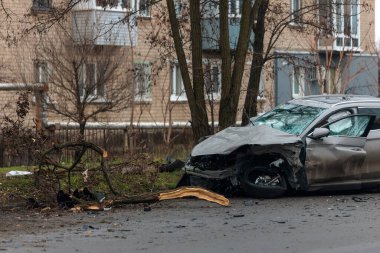 Şiddetli bir kazadan sonra, bir şehir caddesinde meydana gelen çarpışmadan sonra ön yüzünde feci hasar olan gri bir SUV. Kaput buruşmuş, lastik yerinden çıkmış, ön cam kırılmış ve kapı açık ve deforme olmuş..