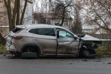 Şiddetli bir kazadan sonra, bir şehir caddesinde meydana gelen çarpışmadan sonra ön yüzünde feci hasar olan gri bir SUV. Kaput buruşmuş, lastik yerinden çıkmış, ön cam kırılmış ve kapı açık ve deforme olmuş..