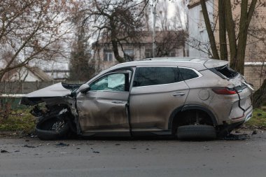 Şiddetli bir kazadan sonra, bir şehir caddesinde meydana gelen çarpışmadan sonra ön yüzünde feci hasar olan gri bir SUV. Kaput buruşmuş, lastik yerinden çıkmış, ön cam kırılmış ve kapı açık ve deforme olmuş..