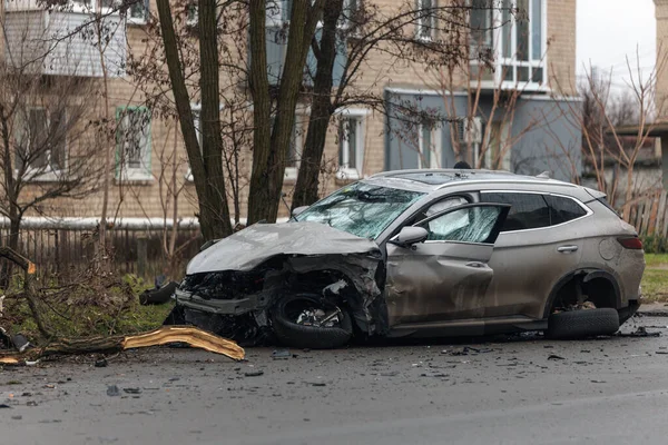 Şiddetli bir kazadan sonra, bir şehir caddesinde meydana gelen çarpışmadan sonra ön yüzünde feci hasar olan gri bir SUV. Kaput buruşmuş, lastik yerinden çıkmış, ön cam kırılmış ve kapı açık ve deforme olmuş..