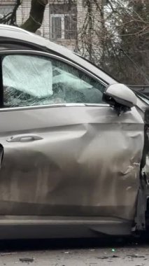 Şiddetli bir kazadan sonra, bir şehir caddesinde meydana gelen çarpışmadan sonra ön yüzünde feci hasar olan gri bir SUV. Kaput buruşmuş, lastik yerinden çıkmış, ön cam kırılmış ve kapı açık ve deforme olmuş..