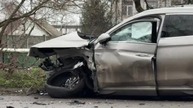 Şiddetli bir kazadan sonra, bir şehir caddesinde meydana gelen çarpışmadan sonra ön yüzünde feci hasar olan gri bir SUV. Kaput buruşmuş, lastik yerinden çıkmış, ön cam kırılmış ve kapı açık ve deforme olmuş..