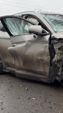 Şiddetli bir kazadan sonra, bir şehir caddesinde meydana gelen çarpışmadan sonra ön yüzünde feci hasar olan gri bir SUV. Kaput buruşmuş, lastik yerinden çıkmış, ön cam kırılmış ve kapı açık ve deforme olmuş..